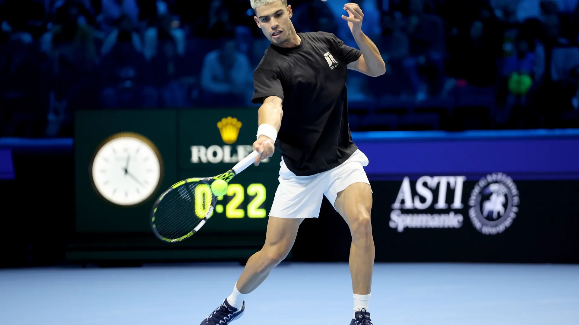 Carlos sfoggia questa nuova pettinatura, biondo platino al centro della testa, scuro-rasata ai lati, e una t-shirt nera, con la sua caricatura disegnata sulla schiena.