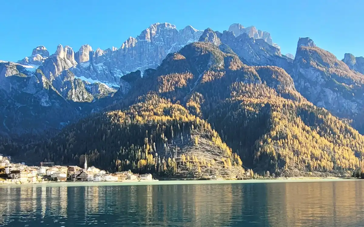Il lago dolomitico con i villaggi sommersi sul fondo: Alleghe, la val Cordevole e l’autunno tra i larici
